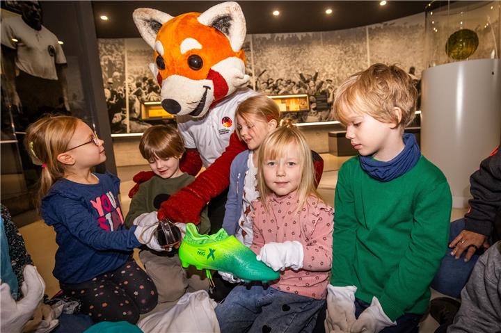 Fußballgeschichte zum Anfassen: Maskottchen Rio zeigt Kindern Fußballschuhe aus verschiedenen Jahrhunderten. Foto: Stephan Schütze